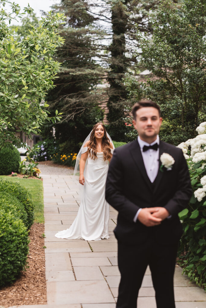 Bride facing groom while his back is turned for the first look outside the Woolverton Inn, photographed by New Jersey and Philadelphia based travel wedding photographer Madison Neumann Photography.