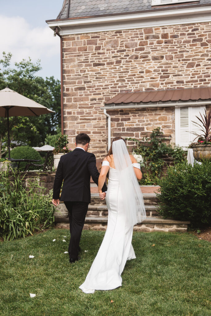 Shot of bride and groom from behind as they exit the ceremony and head towards the reception at The Woolverton Inn, photographed by New Jersey and Philadelphia based travel wedding photographer Madison Neumann Photography.