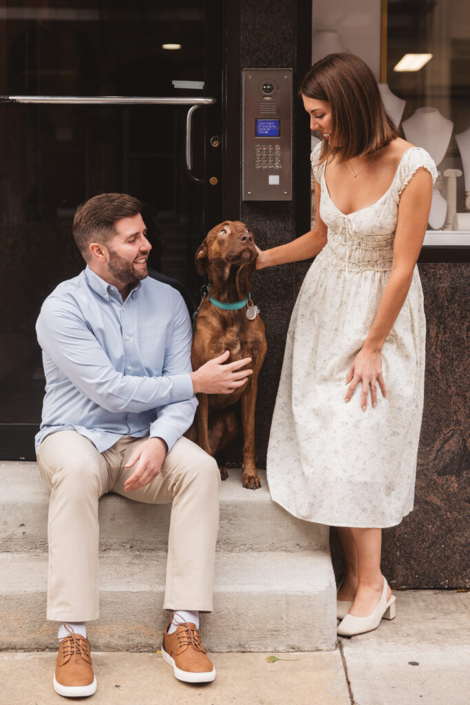 Couple petting their dog Moose on the steps of a jewelry store, photographed by Philadelphia and New Jersey based travel wedding photographer, Madison Neumann Photography.
