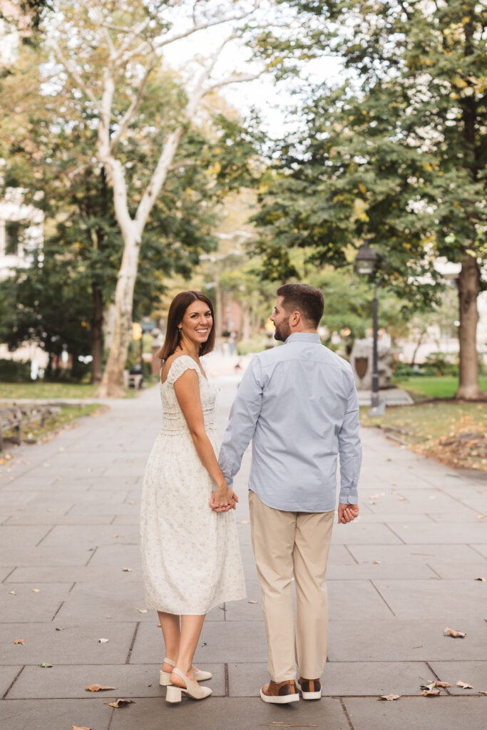 Shot of couple from behind as the future bride looks back at the camera, hand in hand with her future husband, photographed by Philadelphia and New Jersey based travel wedding photographer, Madison Neumann Photography.