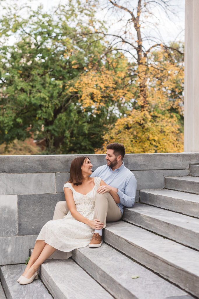 Future bride sits on the step in between the legs of future groom while smiling at each other, photographed by Philadelphia and New Jersey based travel wedding photographer, Madison Neumann Photography.