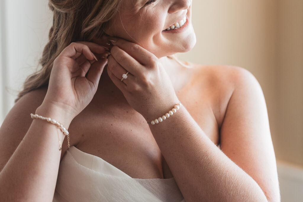 Detail photo of bride putting in her earrings and smiling, photographed by New Jersey and Philadelphia based travel wedding photographer, Madison Neumann Photography.