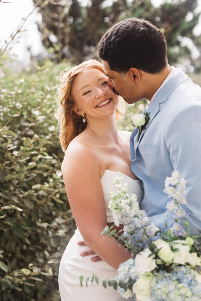 Portrait of bride and groom outside in the Outer Banks, North Carolina as groomer kisses bride on the cheek, making her smile. photographed by New Jersey and Philadelphia based travel wedding photographer, Madison Neumann Photography.