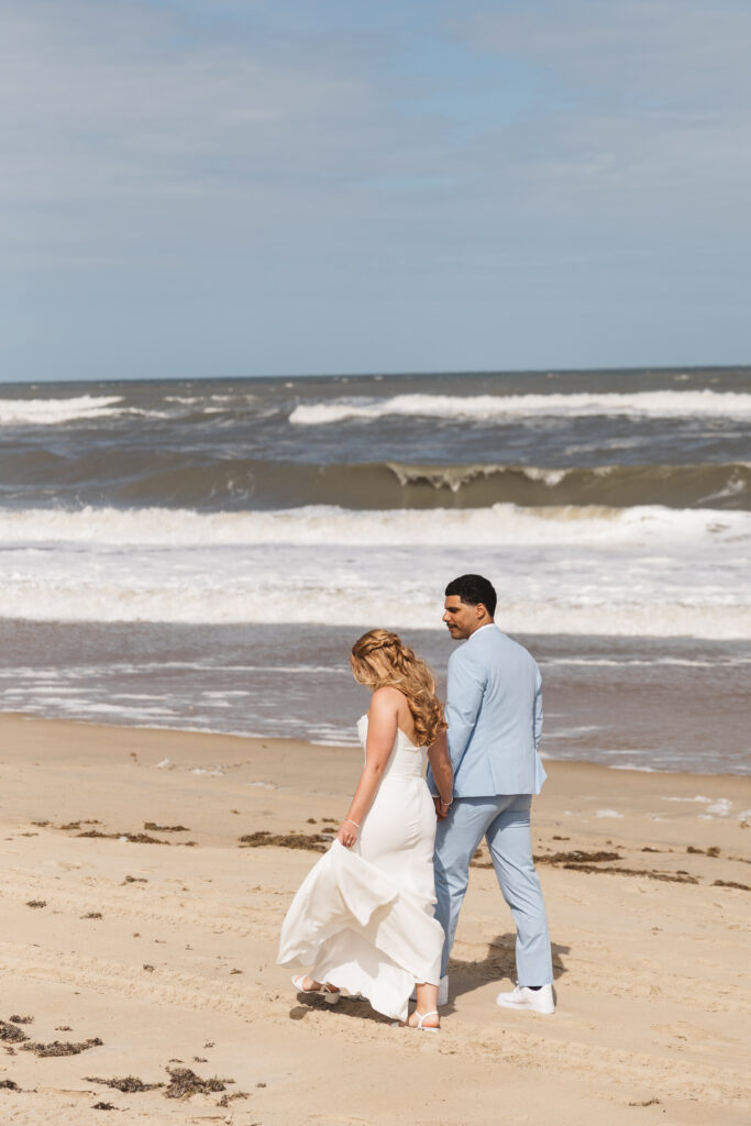 Bride and groom from behind walking on the beaches of Outer Banks, NC hand in hand, photographed by New Jersey and Philadelphia based travel wedding photographer, Madison Neumann Photography.