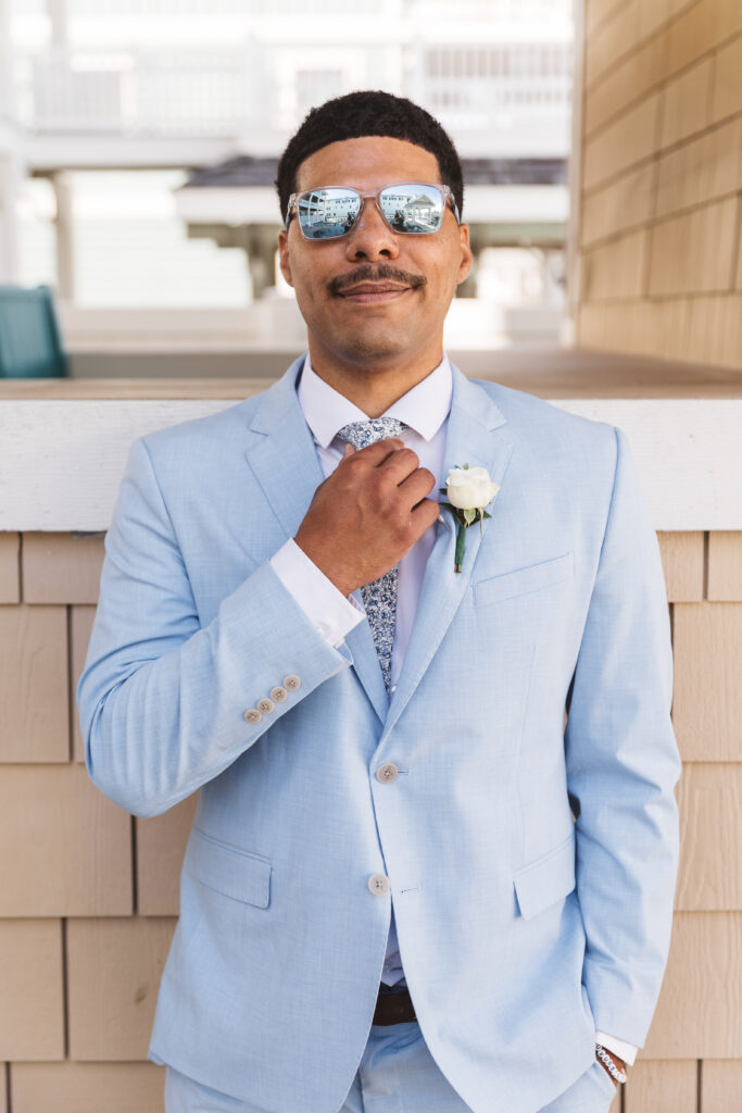 Groom adjusting his tie with matching sunglasses on outside rental in Outer Banks, North Carolina. photographed by New Jersey and Philadelphia based travel wedding photographer, Madison Neumann Photography.