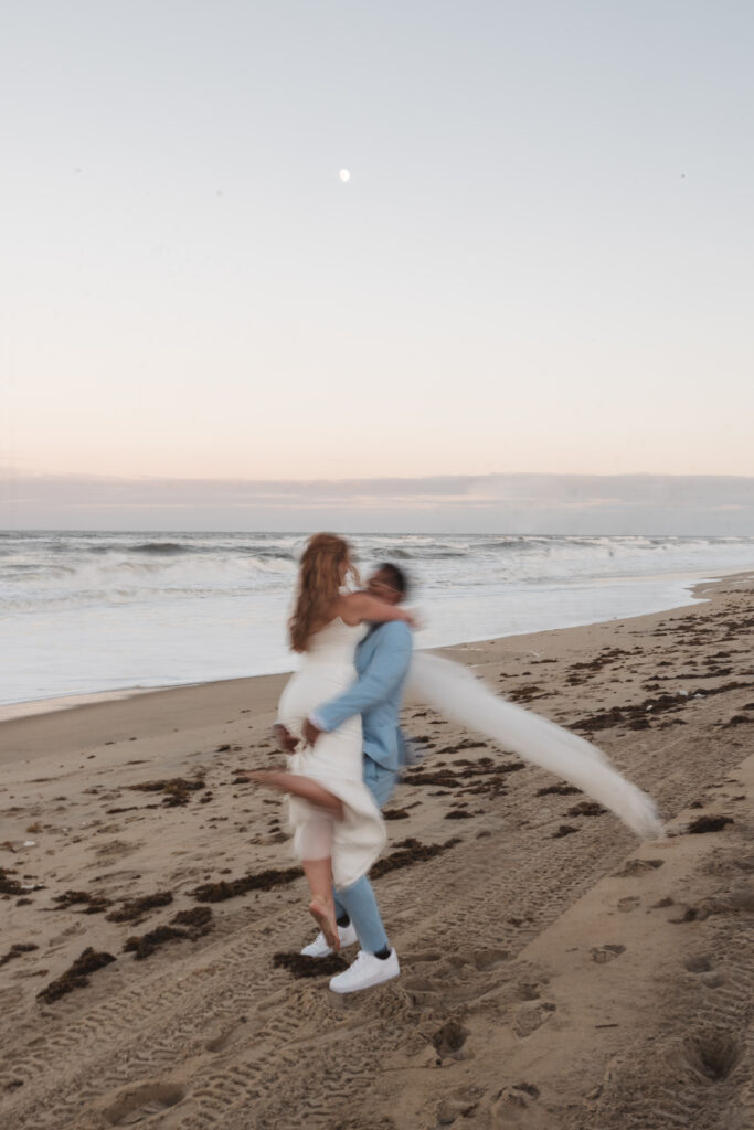 Groom lifting up and spinning his bride in a blur during sunset on the beaches of Outer Banks, North Carolina, photographed by New Jersey and Philadelphia based travel wedding photographer, Madison Neumann Photography.