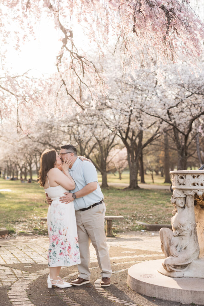 Bride and groom share a kiss by the fountain with the beautiful row of blossoms in the background, photographed by Philadelphia and New Jersey based travel wedding photographer, Madison Neumann Photography.