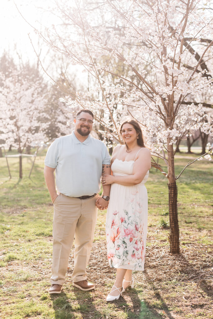 Couple hand in hand with bride-to-be holding her fiancé's arm with beautiful blossom trees in the background, photographed by Philadelphia and New Jersey based travel wedding photographer, Madison Neumann Photography.