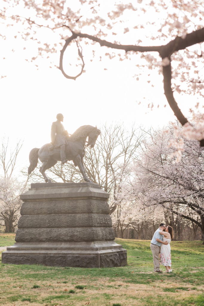 Zoomed out photo of the couple sharing a kiss next to the Meade statue in fairmont park, photographed by Philadelphia and New Jersey based travel wedding photographer, Madison Neumann Photography.