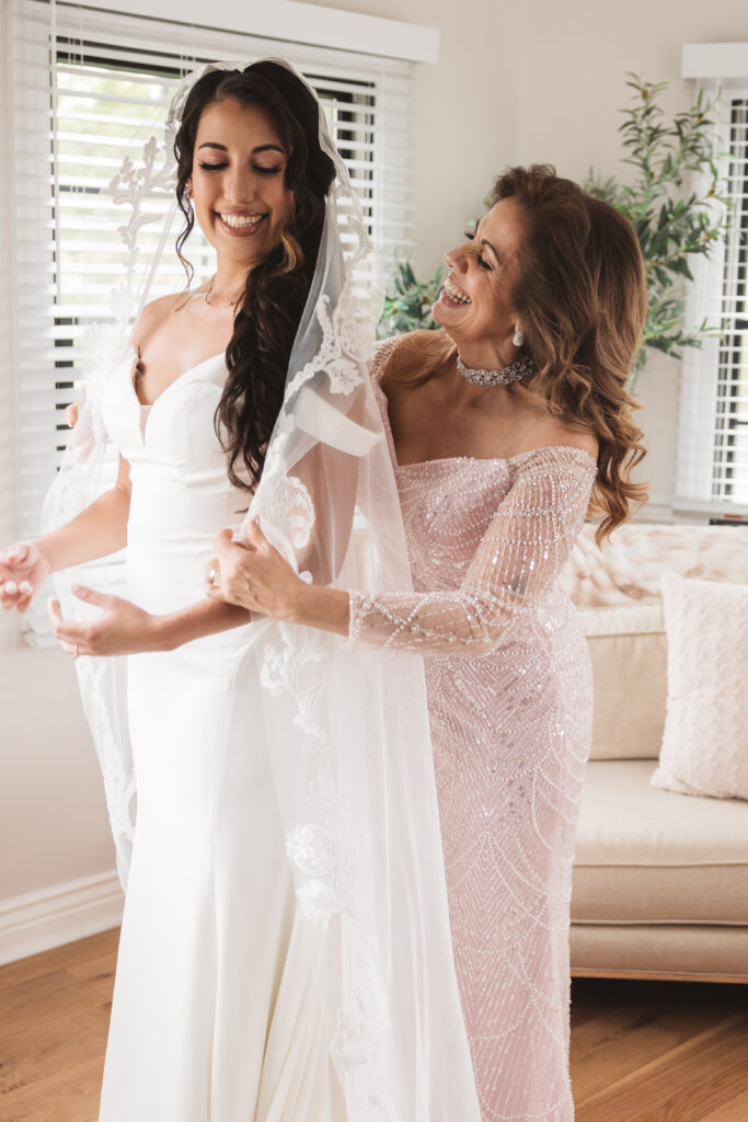 Bride and her mom getting ready and fixing the veil while smiling, photographed by Philadelphia and New Jersey based travel wedding photographer, Madison Neumann Photography.