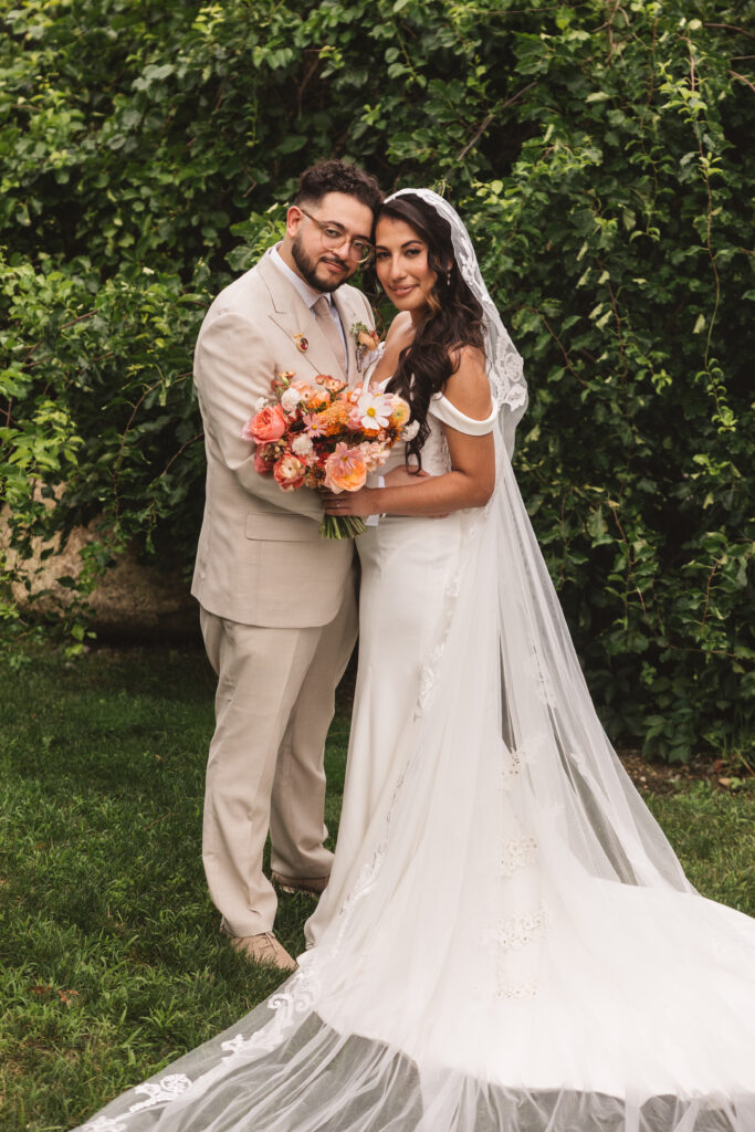 Portrait of bride and groom in front of beautiful green foliage, looking at the camera with their heads resting on one another, photographed by Philadelphia and New Jersey based travel wedding photographer, Madison Neumann Photography.