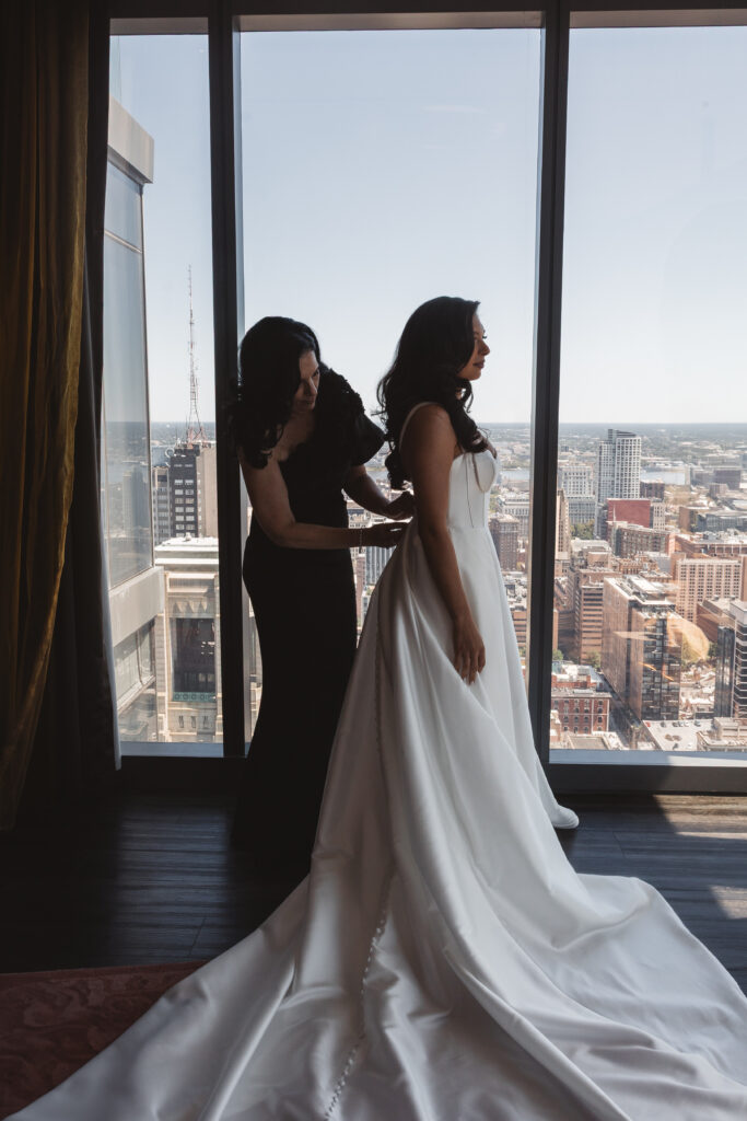 Portrait of the bride and her mother as she gets help buttoning up her dress overlooking the beautiful Philadelphia skyline photographed by Philadelphia and New Jersey based travel wedding photographer, Madison Neumann Photography.