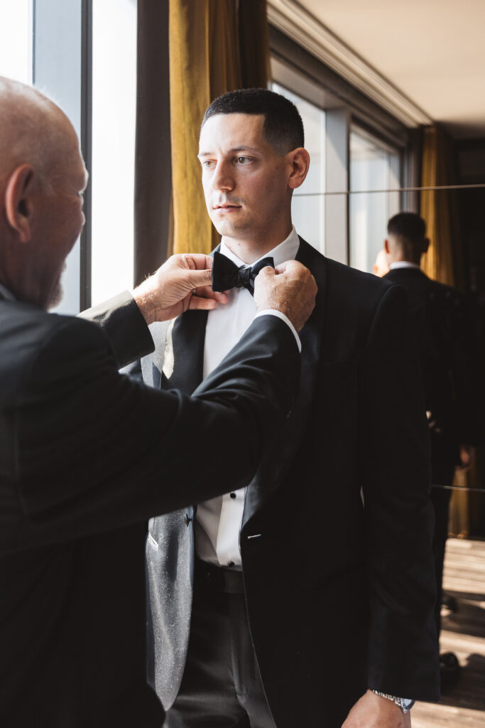 Groom being helped by a loved one to fix his bowtie, photographed by Philadelphia and New Jersey based travel wedding photographer, Madison Neumann Photography.