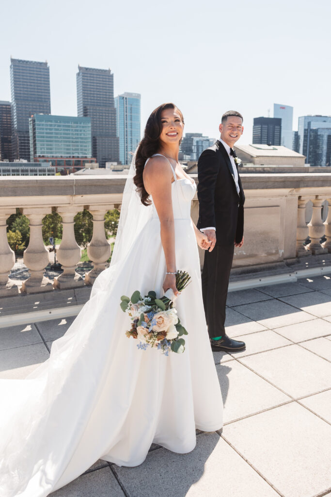 Another shot of the couple holding hands as they look back smiling with the city behind them, photographed by Philadelphia and New Jersey based travel wedding photographer, Madison Neumann Photography.
