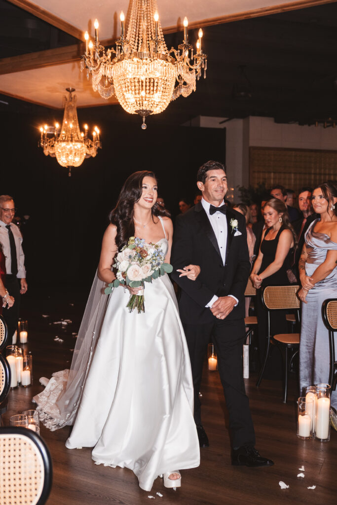 Bride coming down the aisle on her fathers arm with chandeliers hanging in the background, photographed by Philadelphia and New Jersey based travel wedding photographer, Madison Neumann Photography.