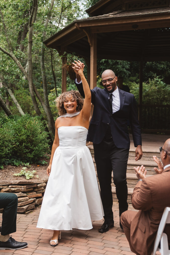 Bride and groom hold their interlocked hands up high as they leave the ceremony with smiles on their faces, photographed by Philadelphia and New Jersey based travel wedding photographer, Madison Neumann Photography.