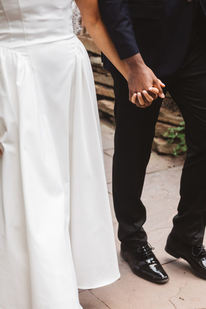 Detail shot of the bride and groom holding hands with contrast of her white dress and his black suit, photographed by Philadelphia and New Jersey based travel wedding photographer, Madison Neumann Photography.