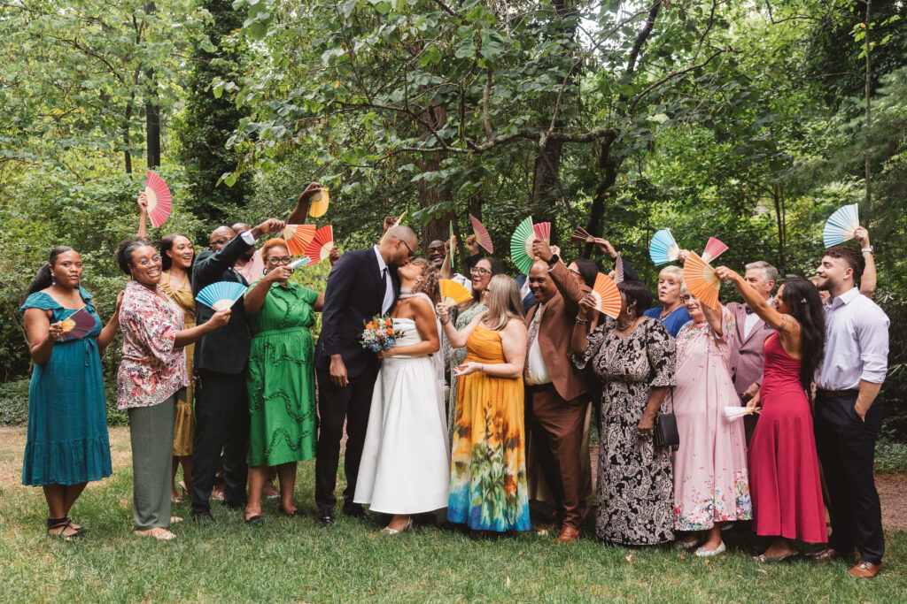 Photo with all of the couples closest friends and family members waving their differently colored fans as the couple kisses, photographed by Philadelphia and New Jersey based travel wedding photographer, Madison Neumann Photography.