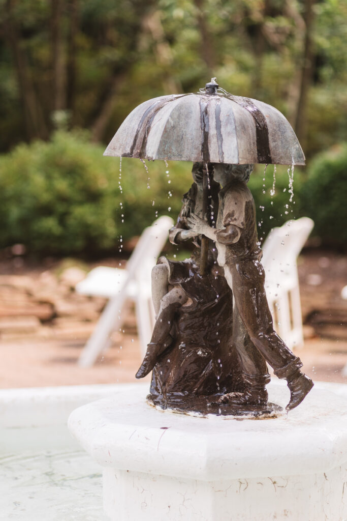 Statue of two people under an umbrella fountain at Sayen Gardens in Hamilton New Jersey, perfect for an intimate elopement ceremony, photographed by Philadelphia and New Jersey based travel wedding photographer, Madison Neumann Photography.