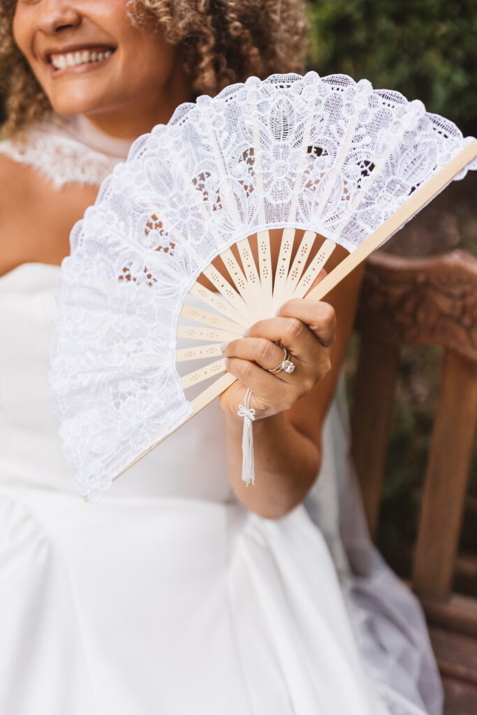 Bride holding up her own fan made of white lace with her ring visible and a big smile, photographed by Philadelphia and New Jersey based travel wedding photographer, Madison Neumann Photography.