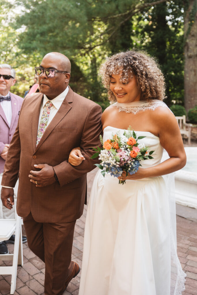 Bride being walked down the aisle by her father who is wearing a nice brown suit before giving her away, photographed by Philadelphia and New Jersey based travel wedding photographer, Madison Neumann Photography.