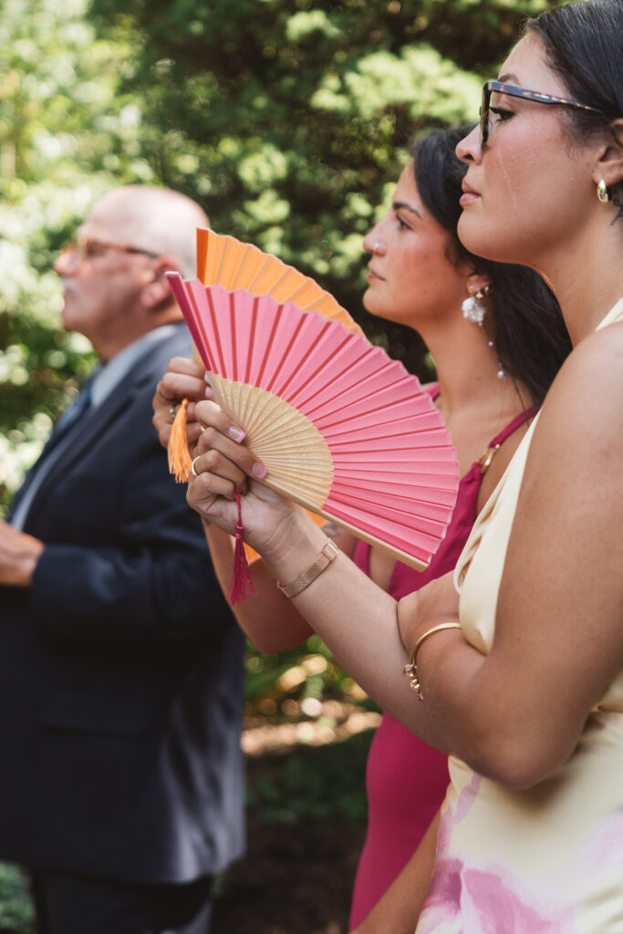 Two young female guests are pictured with tear-stained cheeks and fanning themselves as they listen to the couples vows, photographed by Philadelphia and New Jersey based travel wedding photographer, Madison Neumann Photography.
