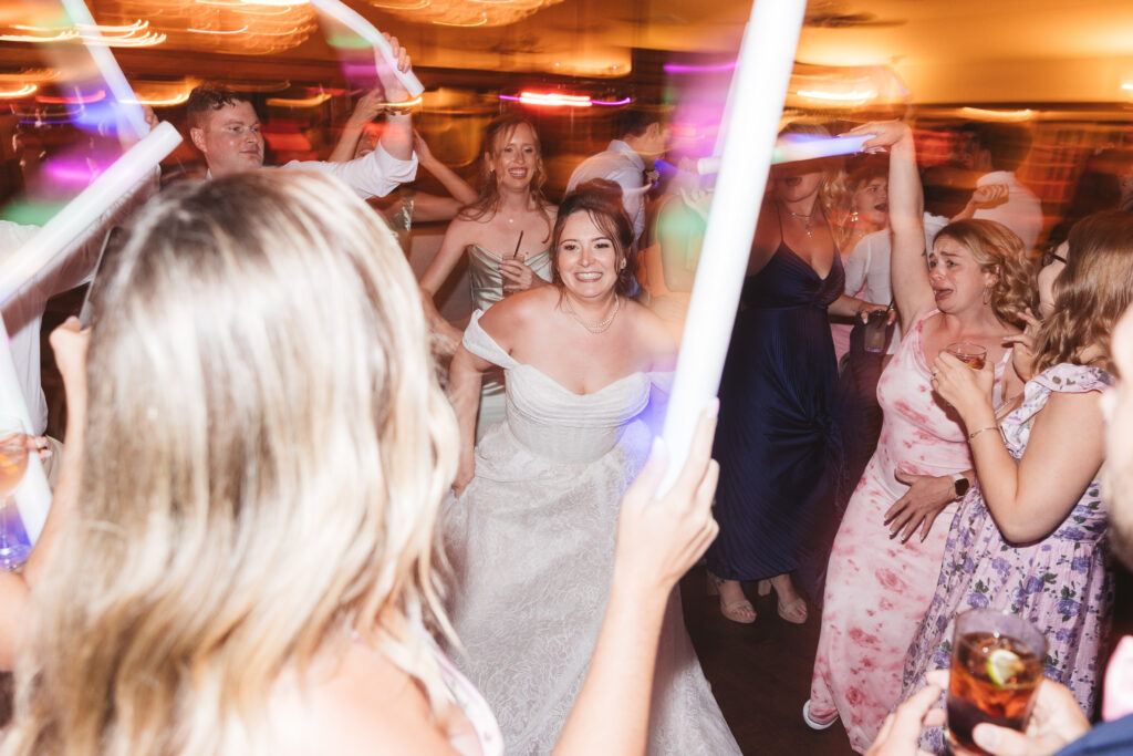 Bride on the dance floor surrounded by a blurred glow of glowsticks held by guests, photographed by Philadelphia and New Jersey based travel wedding photographer, Madison Neumann Photography.