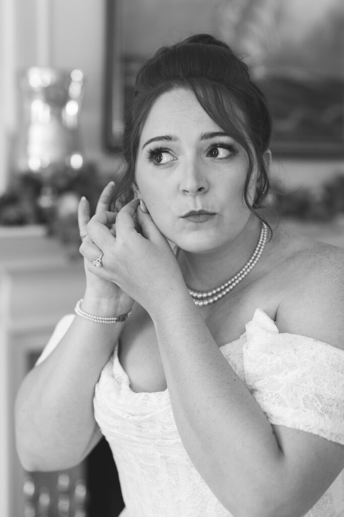 Black and white photo of the beautiful bride putting her earrings in while getting ready, photographed by Philadelphia and New Jersey based travel wedding photographer, Madison Neumann Photography.