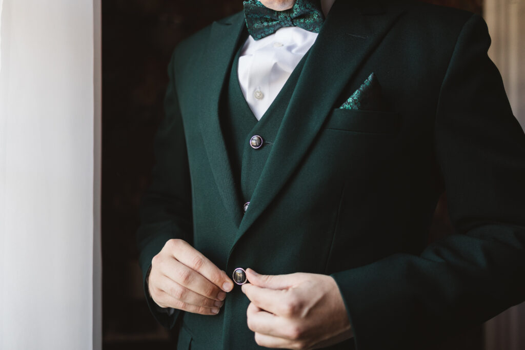 Detail shot of the grooms green suit as he buttons his jacket, photographed by Philadelphia and New Jersey based travel wedding photographer, Madison Neumann Photography.