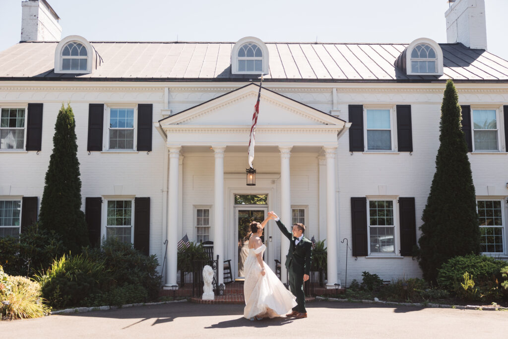 Groom spins his bride in front of the White Lion Manor in Connecticut, photographed by Philadelphia and New Jersey based travel wedding photographer, Madison Neumann Photography.