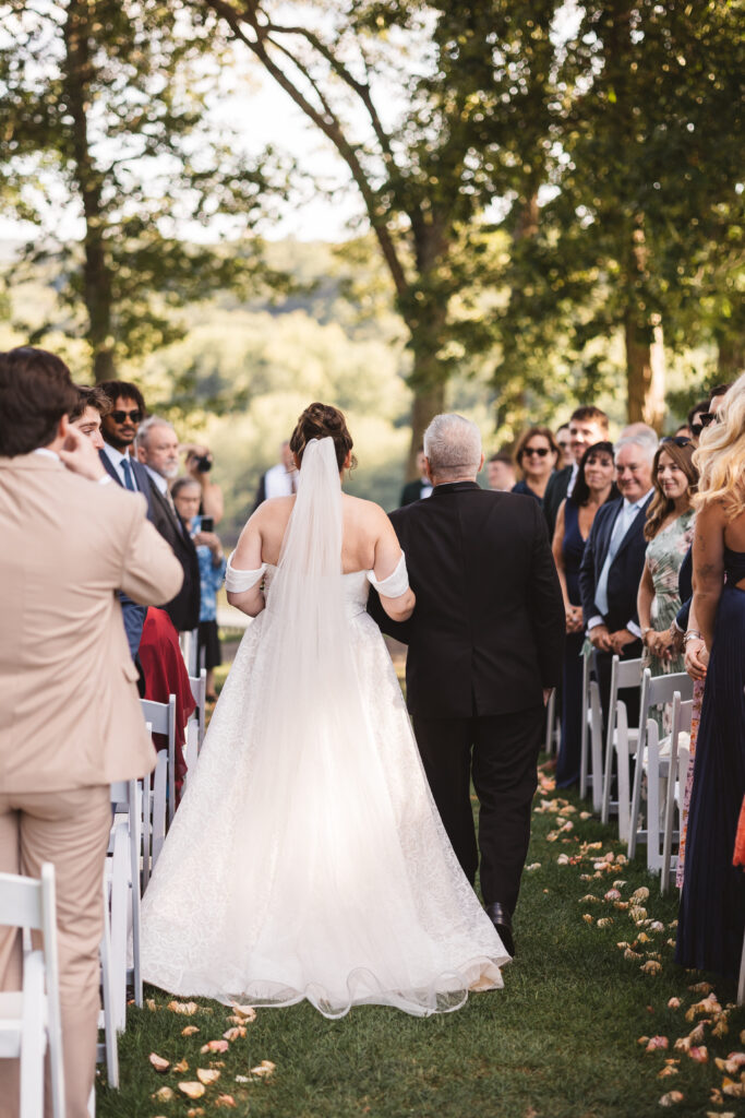 Photo from behind the bride and her father as they make their way down the aisle surrounded by friends and family, photographed by Philadelphia and New Jersey based travel wedding photographer, Madison Neumann Photography.
