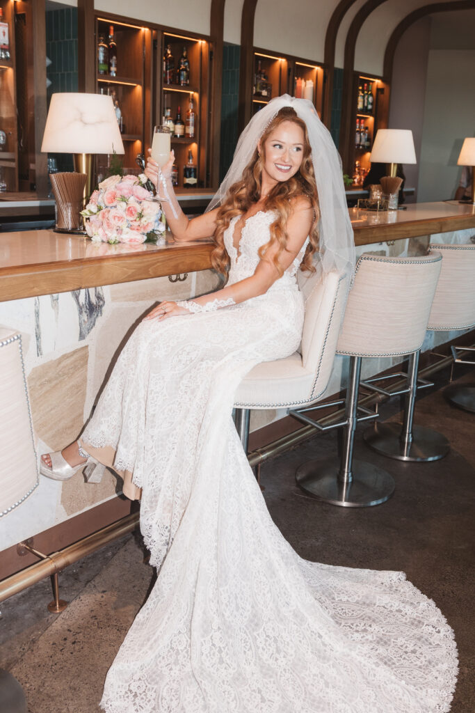 Portrait of bride sitting at the pink bar with a drink and her bouquet, photographed by Philadelphia and New Jersey based travel wedding photographer, Madison Neumann Photography.