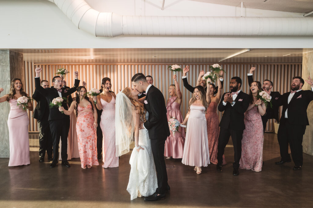 Bride and groom kiss while their wedding party cheers them on from behind, photographed by Philadelphia and New Jersey based travel wedding photographer, Madison Neumann Photography.
