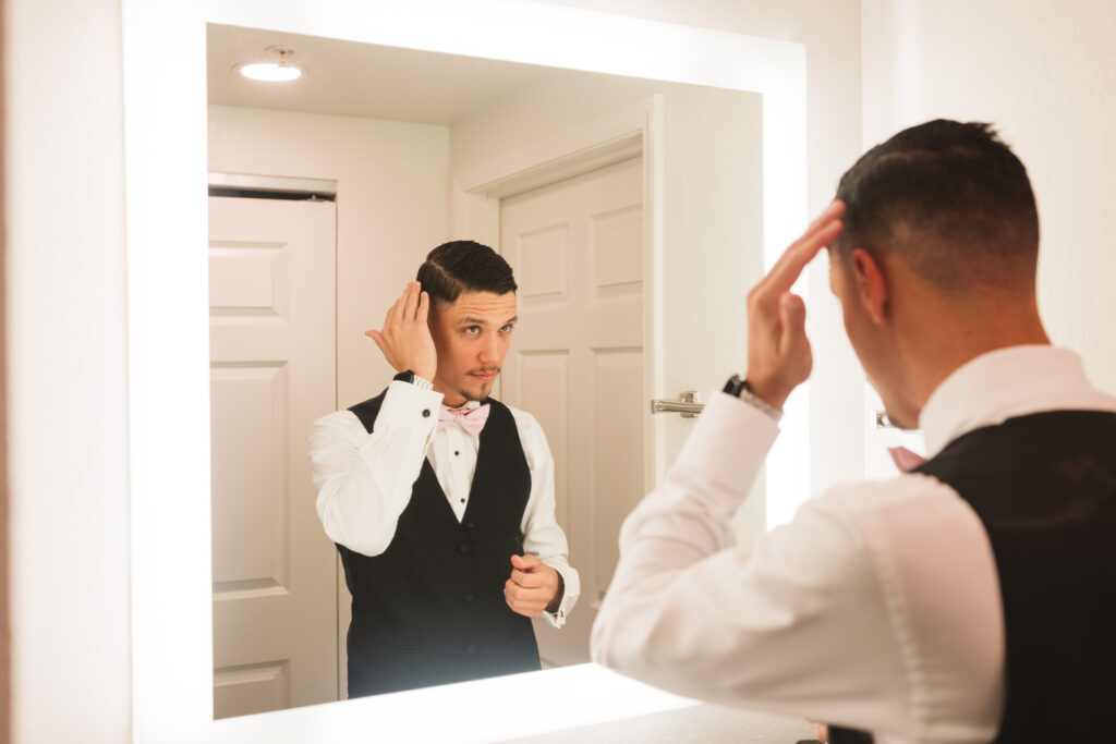 Groom fixing his hair in the mirror while getting ready in his suite, photographed by Philadelphia and New Jersey based travel wedding photographer, Madison Neumann Photography.