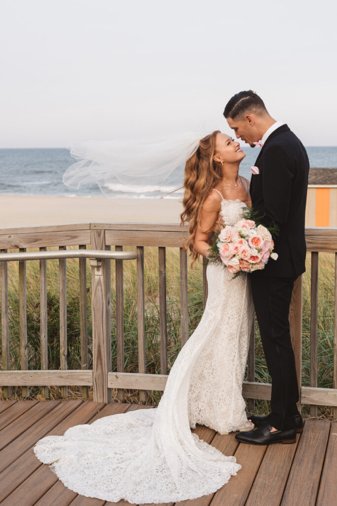 Portrait of bride and groom in front of the beach as the brides veil flows in the wind, photographed by Philadelphia and New Jersey based travel wedding photographer, Madison Neumann Photography.