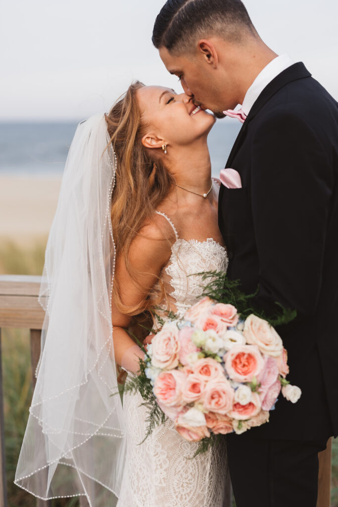 Bride smiling into a kiss with her husband in front of the beach in Long Branch, NJ, photographed by Philadelphia and New Jersey based travel wedding photographer, Madison Neumann Photography.