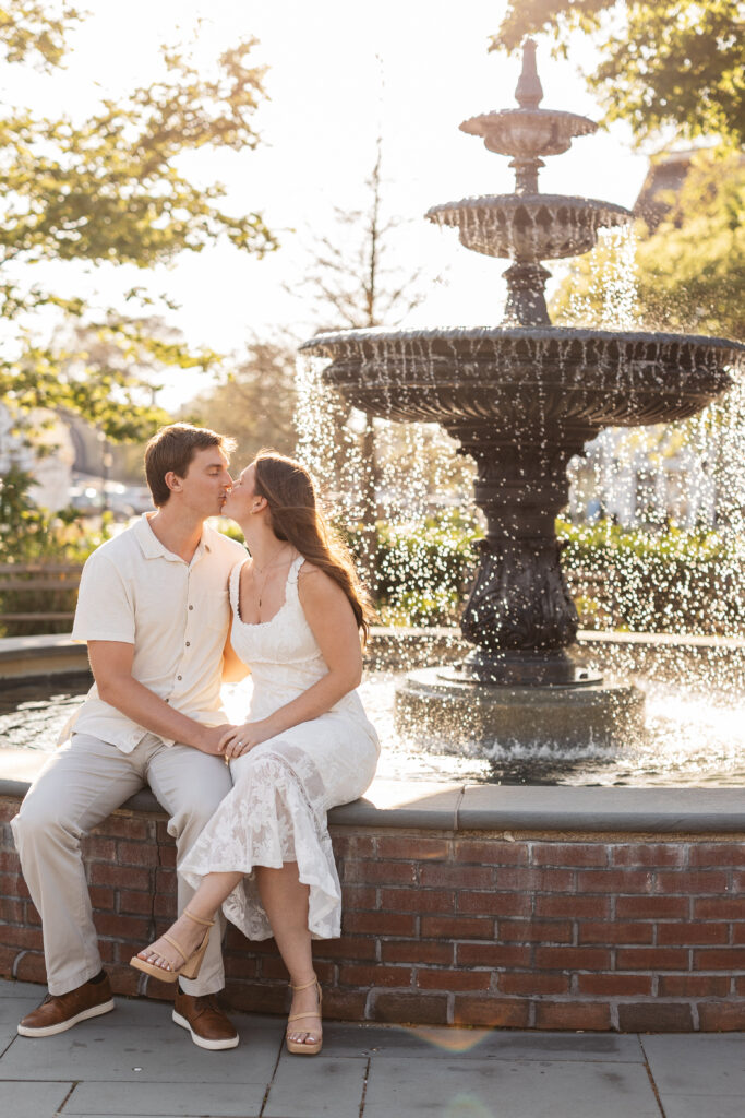 Newly engaged couple shared a kiss while sitting on a fountain in Cape May Washington Square Mall, photographed by Philadelphia and New Jersey based travel wedding photographer, Madison Neumann Photography.