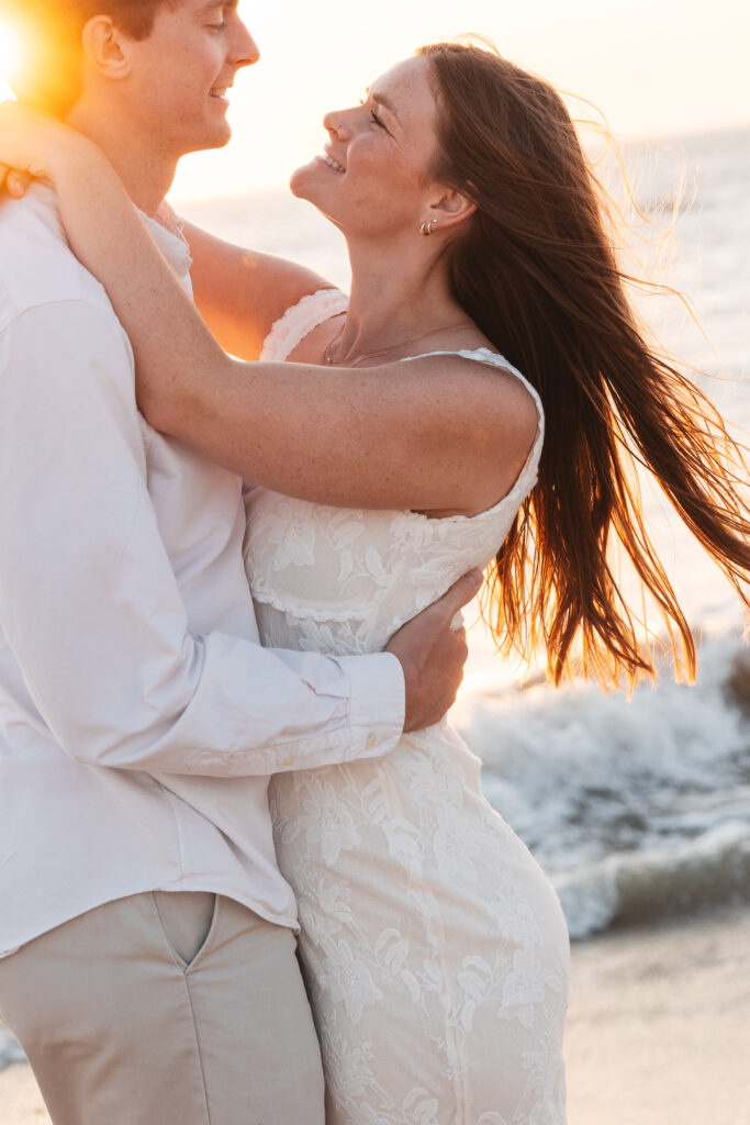 Future groom holds his fiancé close to his chest as they exchange an intimate moment illuminated by the sunset, photographed by Philadelphia and New Jersey based travel wedding photographer, Madison Neumann Photography.