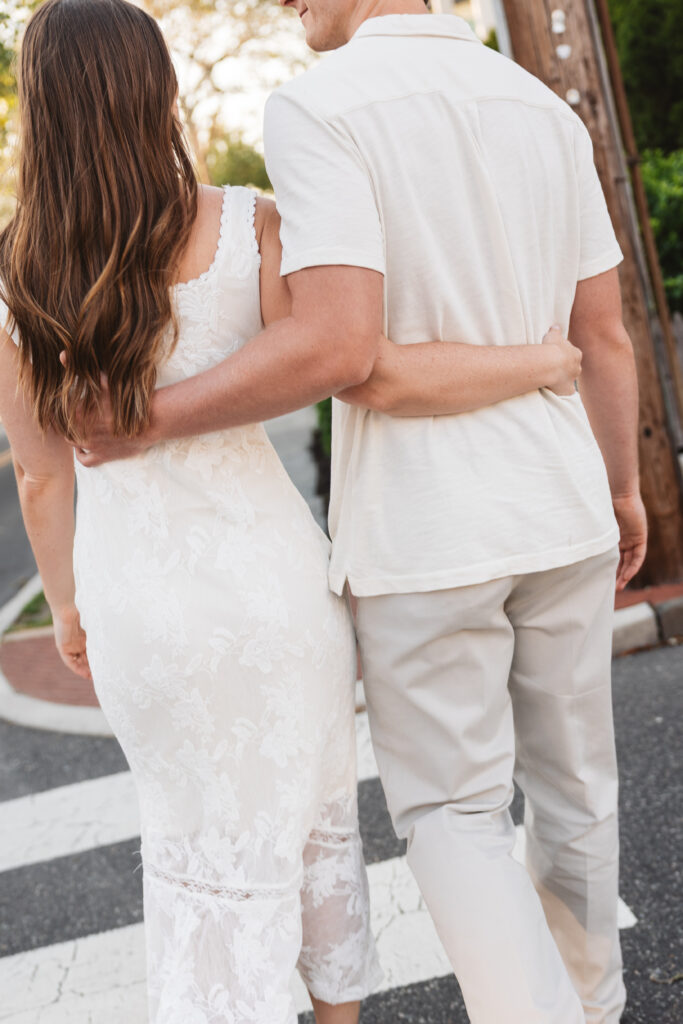 Shot from behind the happy couple as they link their arms behind each other as they cross the street in Cape May, NJ. Photographed by Philadelphia and New Jersey based travel wedding photographer, Madison Neumann Photography.
