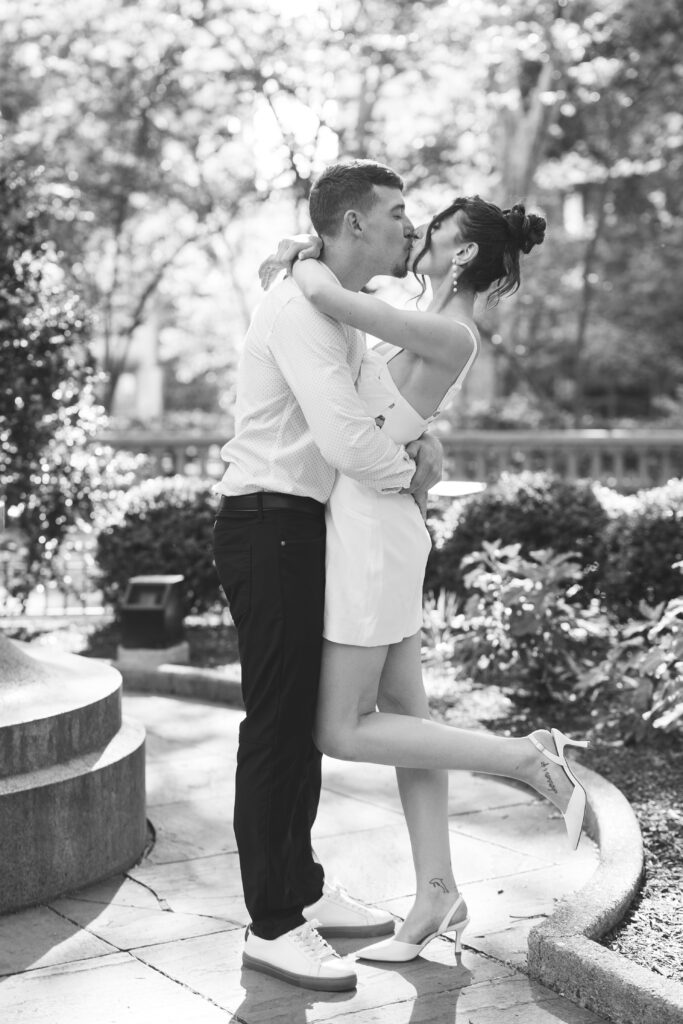 Black and white photo of the happy couple hugging and kissing with the brides foot popped out for a princess kiss, photographed by Philadelphia and New Jersey based travel wedding photographer, Madison Neumann Photography.