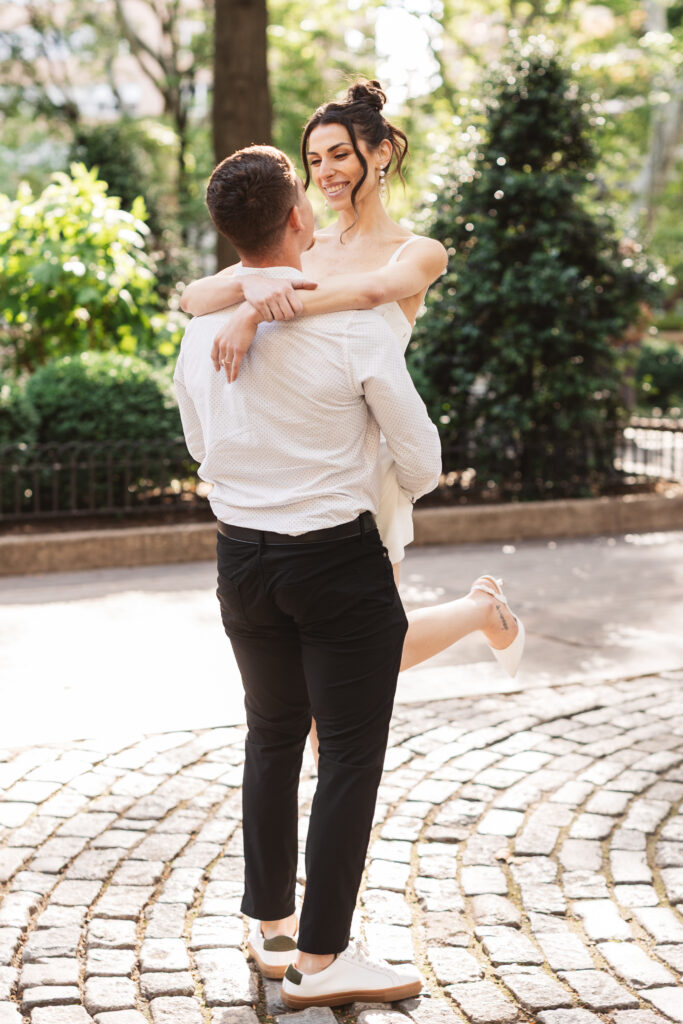 Bride held up in the air by her fiancé while smiling at him on the cobblestone in Philadelphia, photographed by Philadelphia and New Jersey based travel wedding photographer, Madison Neumann Photography.