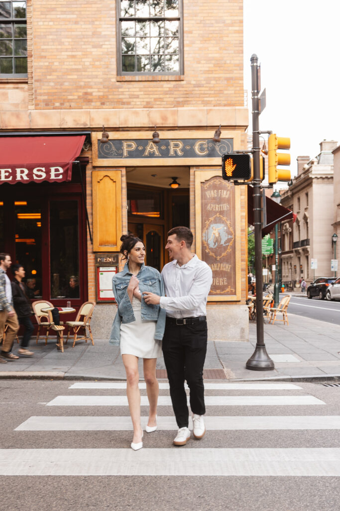 Happy couple crosses the street together with the bride holding a jean jacket over her shoulders as they smile at each other, photographed by Philadelphia and New Jersey based travel wedding photographer, Madison Neumann Photography.