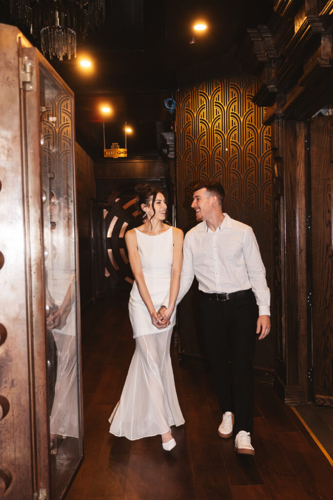 Mrs. and Mr. to be hold hands and smile at one another walking through the hallway of a bar in Philadelphia, photographed by Philadelphia and New Jersey based travel wedding photographer, Madison Neumann Photography.