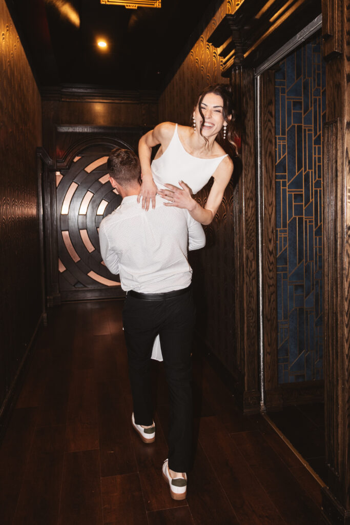 Groom hold his fiancé over his shoulder and walks through the hallway as she smiles at the camera, photographed by Philadelphia and New Jersey based travel wedding photographer, Madison Neumann Photography.