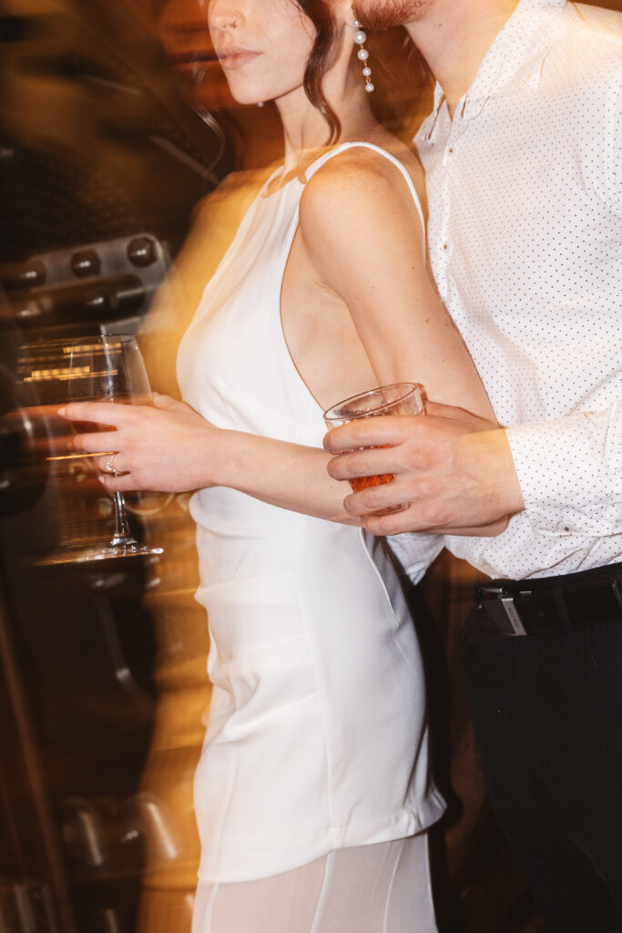 Faceless blurred shot of bride leaning against her fiancé with drinks in hand and a gold blue over the bride, photographed by Philadelphia and New Jersey based travel wedding photographer, Madison Neumann Photography.