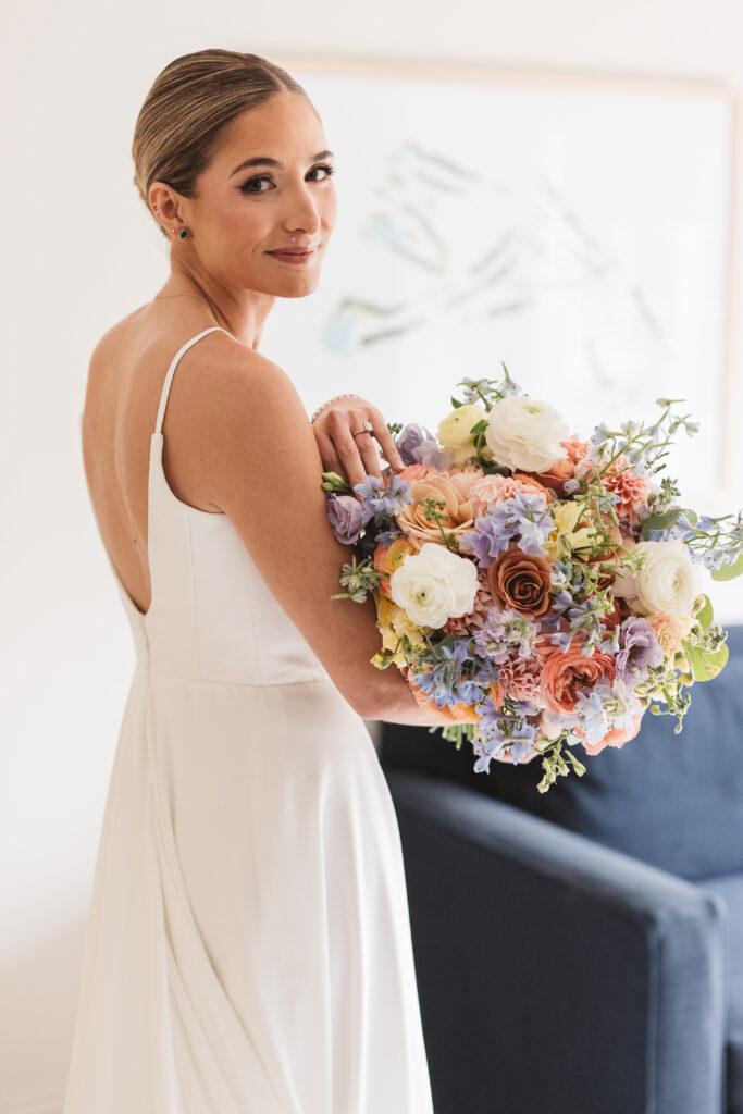Beautiful bride shows off her bouquet and looks over her shoulder in her wedding dress, photographed by Philadelphia and New Jersey based travel wedding photographer, Madison Neumann Photography.