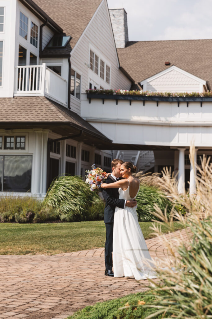 Bride holds her bouquet around her grooms shoulders in front of LBI National, photographed by Philadelphia and New Jersey based travel wedding photographer, Madison Neumann Photography.