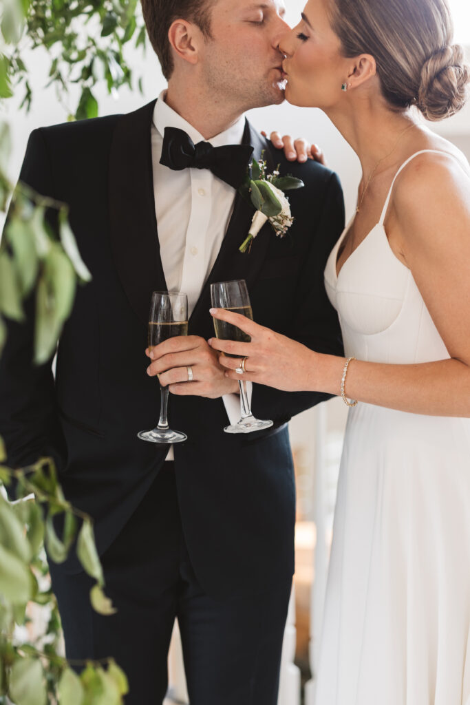 Bride and groom share a kiss as they hold champagne glasses, photographed by Philadelphia and New Jersey based travel wedding photographer, Madison Neumann Photography.