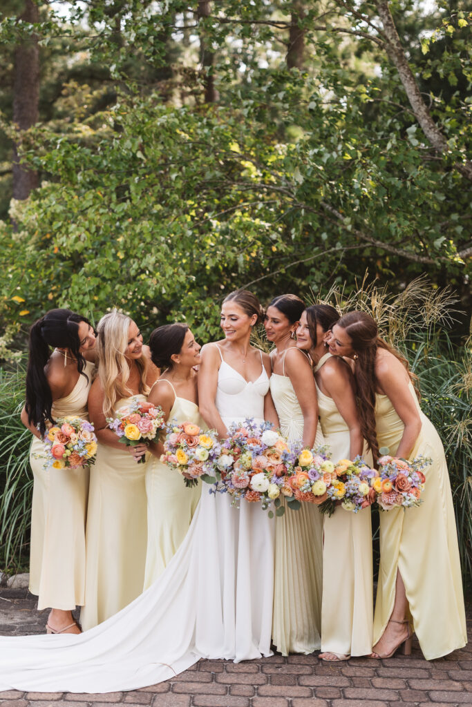 Bride and her bridesmaids smile at one another in their beautiful pale yellow dresses and their matching bouquets, photographed by Philadelphia and New Jersey based travel wedding photographer, Madison Neumann Photography.