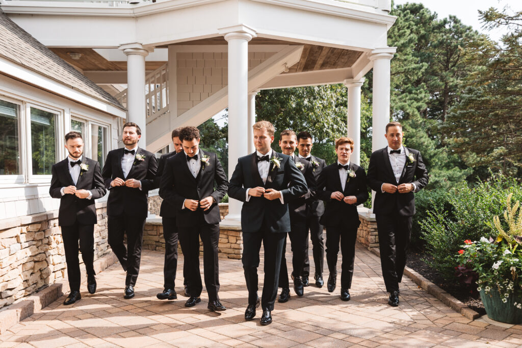 Groom and his groomsmen walking towards the camera and buttoning their jackets outside LBI National, photographed by Philadelphia and New Jersey based travel wedding photographer, Madison Neumann Photography.